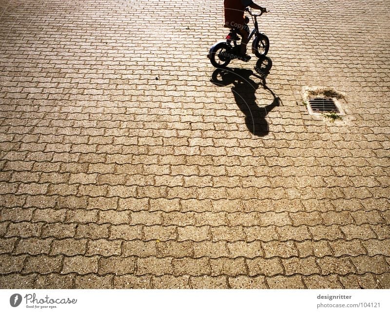 Trial and ... Fahrrad fahren Fahrradfahren Kinderfahrrad Kopfsteinpflaster Fußgängerzone üben Beginn Spielen Rad Schatten Junge Straße Wege & Pfade Stein