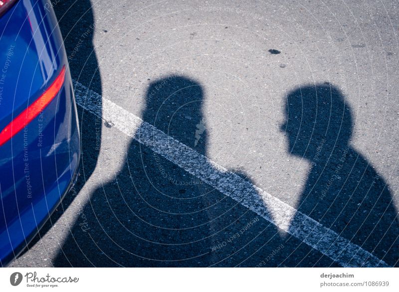 Begegnung auf einem Parkplatz. Zwei Schatten, in der Mitte ein weißer Streifen und links die Rückseite von einem blauen Auto. Freude ruhig maskulin Senior