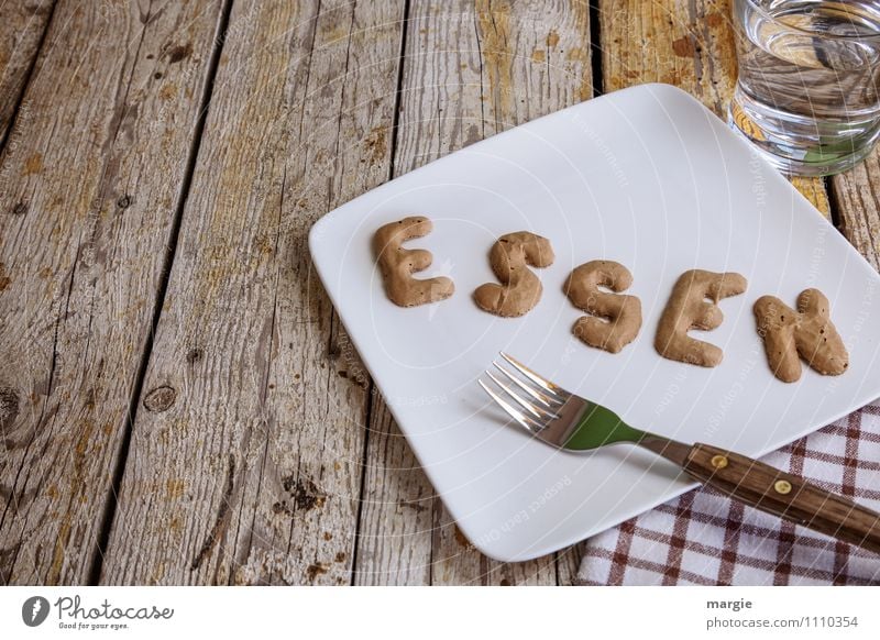 Die Buchstaben ESSEN auf einem Teller mit Gabel, Serviette, einem Glas Wasser auf einem rustikalen Holztisch Ernährung Frühstück Mittagessen Abendessen Picknick