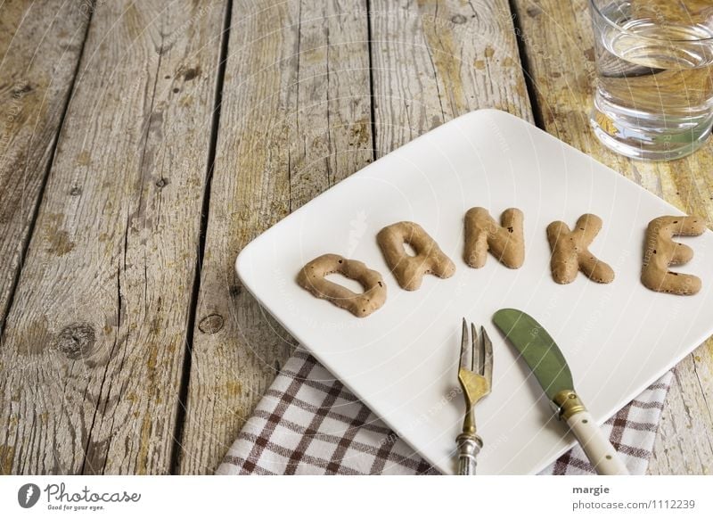 Die Buchstaben DANKE auf einem Teller mit Serviette, Messer, Gabel und einem Wasserglas auf einem rustikalem Holztisch Lebensmittel Frühstück Mittagessen