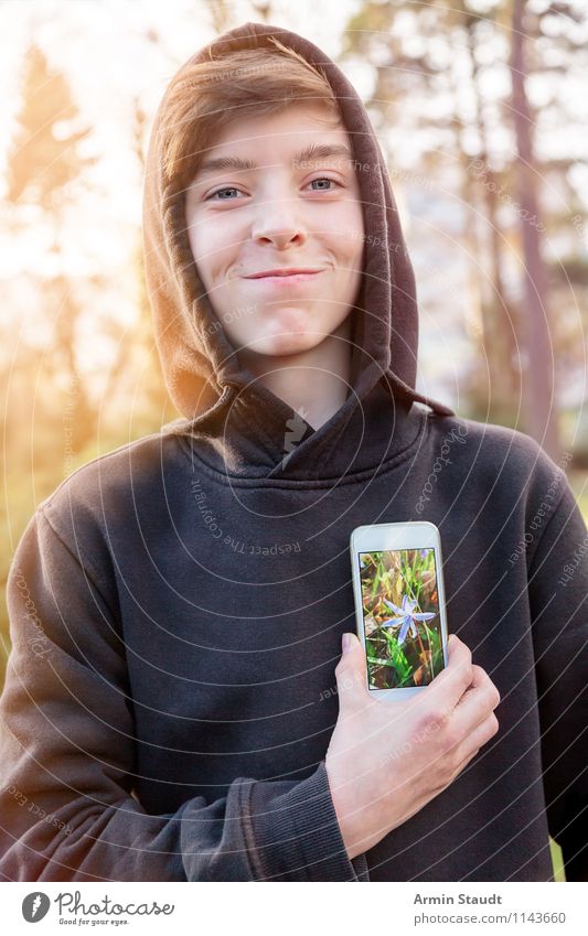 Lächelnder junger Mann hält sich ein Handy mit einem Blumenfoto for das Herz Lifestyle Stil Design Telekommunikation PDA Technik & Technologie Mensch maskulin