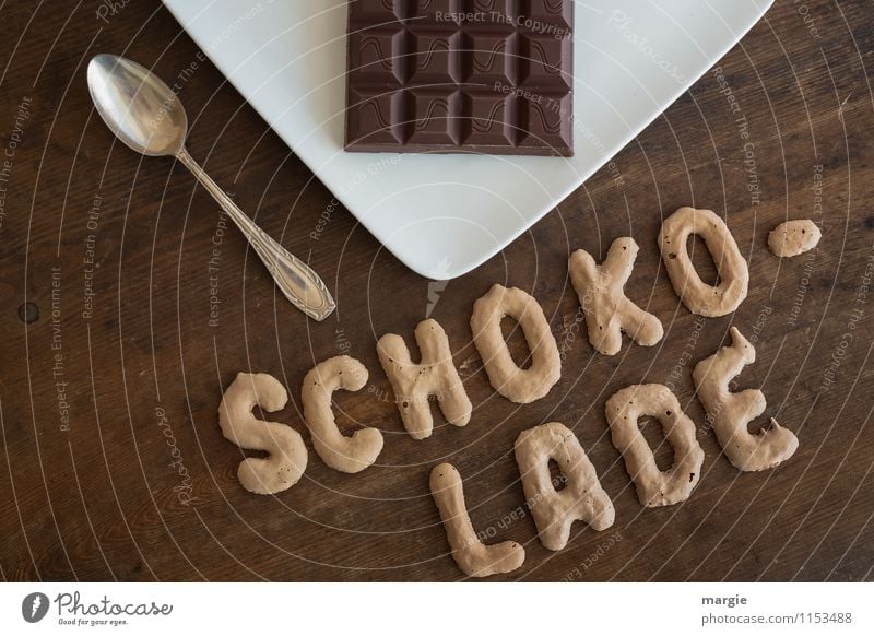 Die Buchstaben SCHOKOLADE auf einem rustikalen Holztisch darüber ein Teller mit einer Tafel Schokolade und ein Teelöffel Lebensmittel Milcherzeugnisse Dessert
