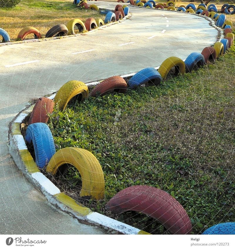 bunte Reifen als Schutz an einer kurvigen Kartbahn und einer Wiese Autorennen Formel 1 Rennbahn Geschwindigkeit fahren Beton Ecke Silhouette Grenze gefährlich