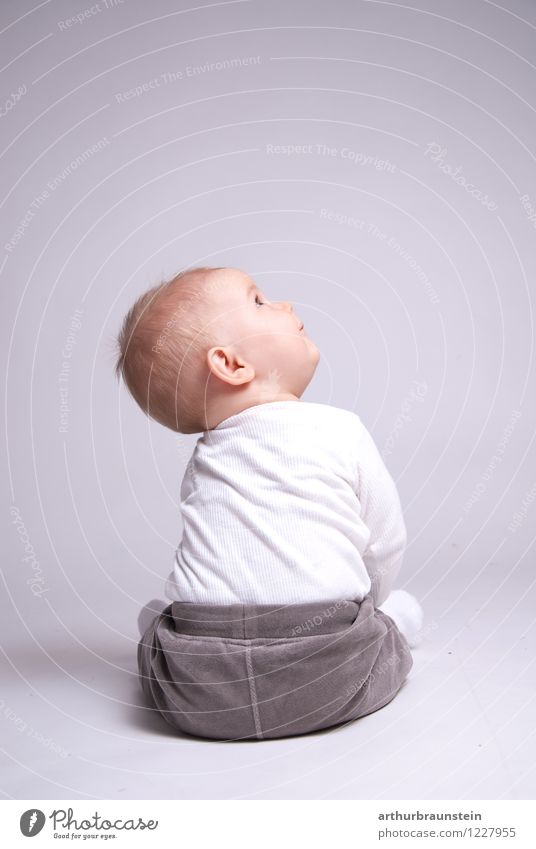 Baby sitzt am weißen Boden im Fotostudio vor weißem Hintergrund und schaut nach oben Glück Kindererziehung Kindergarten Mensch maskulin Kleinkind Kindheit Leben