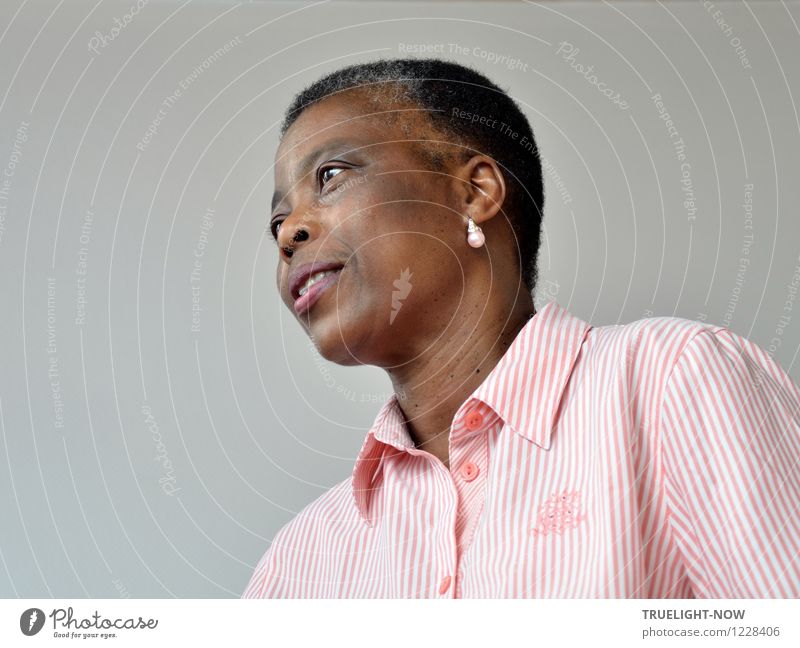 Schöne Afrikanerin aus Togo mit ganz kurzen Haaren, leicht geöffnetem Mund, einem Ohrring mit Perle in einem weiss rosa gestreiften feinen Oberhemd mit Kragen von unten im Halbprofil