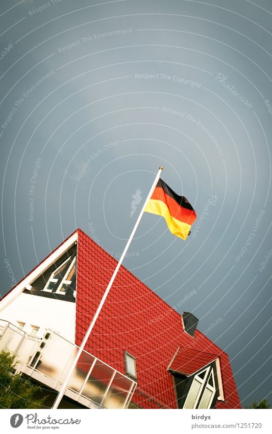 Deutschlandfahne an einem Fahnenmast vor einem neuen Einfamilienhaus in Deutschland. Schief Deutsche Flagge Haus Gewitterwolken Wind Patriotismus deutsch Neubau