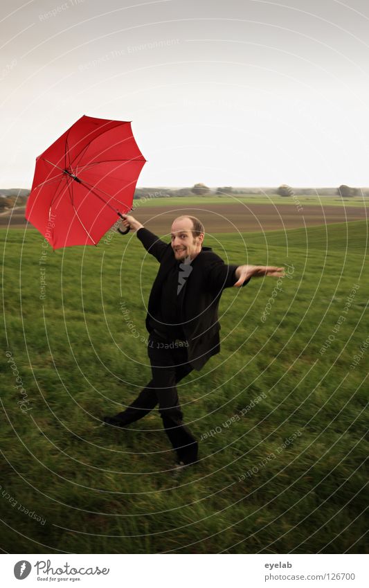Eiernacken Mann Regenschirm Feld Landwirtschaft Wiese Ebene Anzug grün rot schwarz Kerl Grimasse Akrobatik Kunst Horizont Zirkus improvisieren Tanzen Spielen