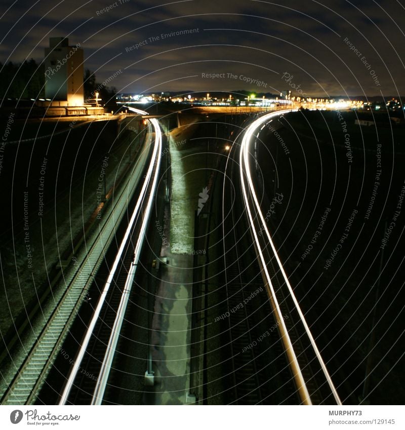 Züge in der Nacht Eisenbahn Gleise Langzeitbelichtung Stadt Silo Güterwaggon Güterzug Schnellzug Leuchtspur Licht Wolken Baum Lampe Horizont grau schwarz gelb