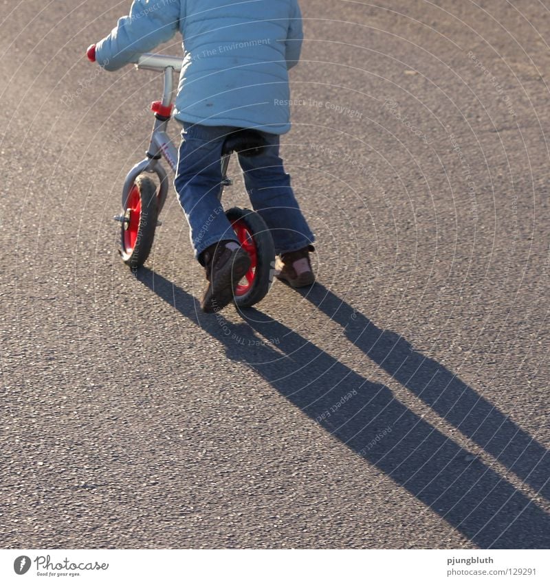 lauf, rad! Kind Licht Asphalt Februar Gegenlicht Zufriedenheit üben Spielen Spaziergang Schatten Straße lernen Kinderfahrrad
