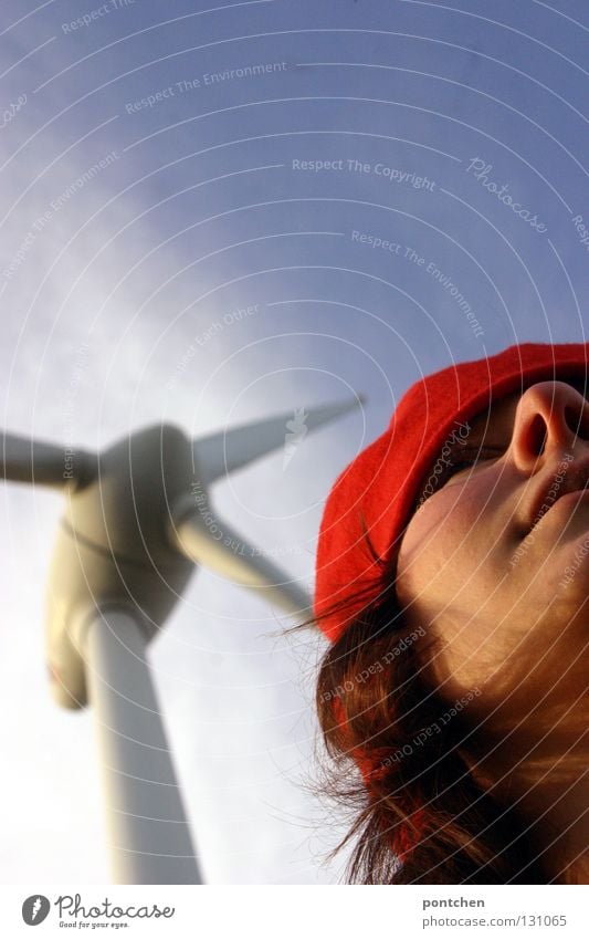 Eine frau mit roter Mütze steht vor einem Windrad. Klimawandel. Alternative Stromgewinnung. Erneuerbare Energie Haare & Frisuren Industrie Energiewirtschaft