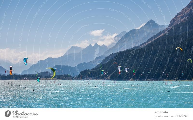 Berglandschaft mit vielen Kitesurfern und Windsurfern, die sich in einem See bewegen. Sie nutzen den Wind, um ihre Bretter auf dem Wasser zu bewegen. Berge sind als Hintergrund an einem sonnigen Tag.