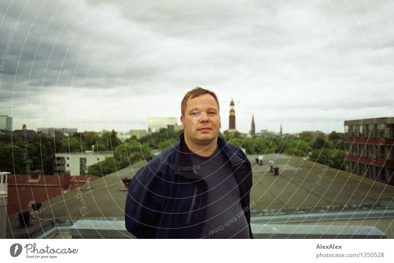 Junger Mann steht auf einem Dach in Hamburg Erwachsene 30-45 Jahre Wolken Skyline Stadt Michaeliskirche Jacke kurzhaarig beobachten Blick ästhetisch frei