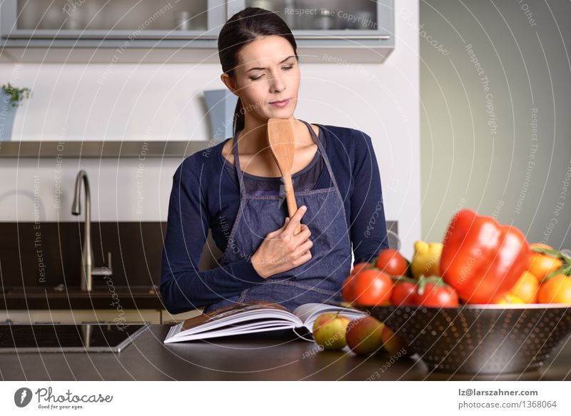 Frau, die Schöpflöffel beim Ablesen eines Kochbuchs hält Gemüse Frucht Ernährung Schalen & Schüsseln Gesicht Küche Gastronomie Erwachsene 1 Mensch 30-45 Jahre