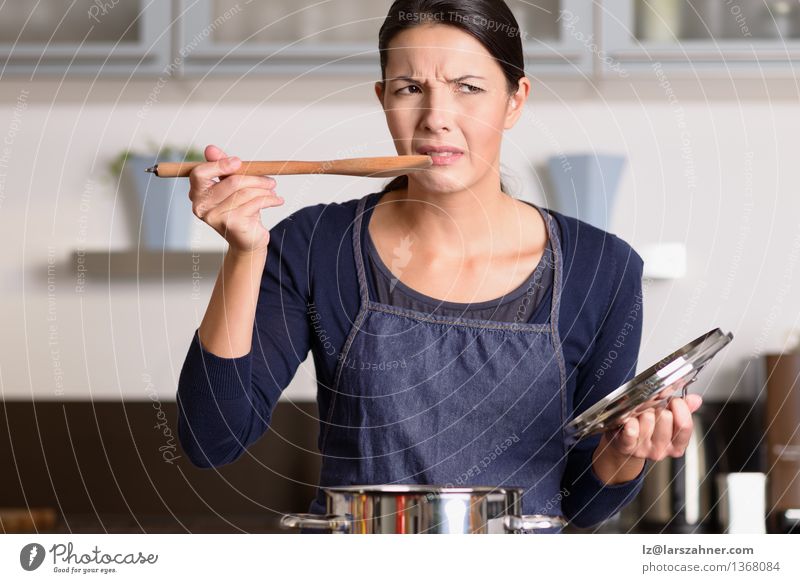Junger Koch, der ihr Lebensmittel mit einer Grimasse schmeckt Abendessen Topf Löffel Gesicht Küche Frau Erwachsene 1 Mensch 30-45 Jahre heiß Wut attraktiv