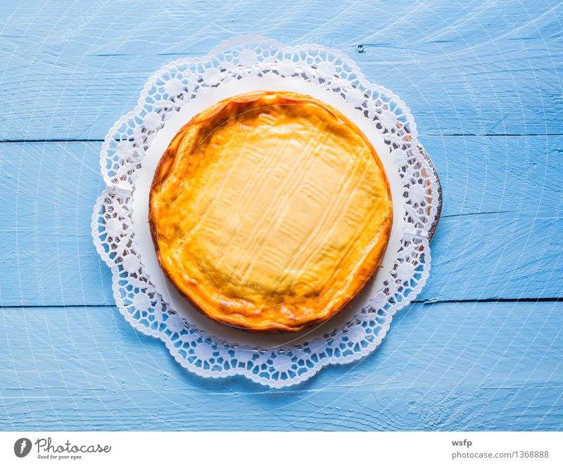 Käsekuchen auf blauem Holz mit Tortenspitze Kuchen Dessert Quarkkuchen Quarktorte Backwaren Biskuit Holztisch rustikal Vogelperspektive Süßwaren rund 1 backen