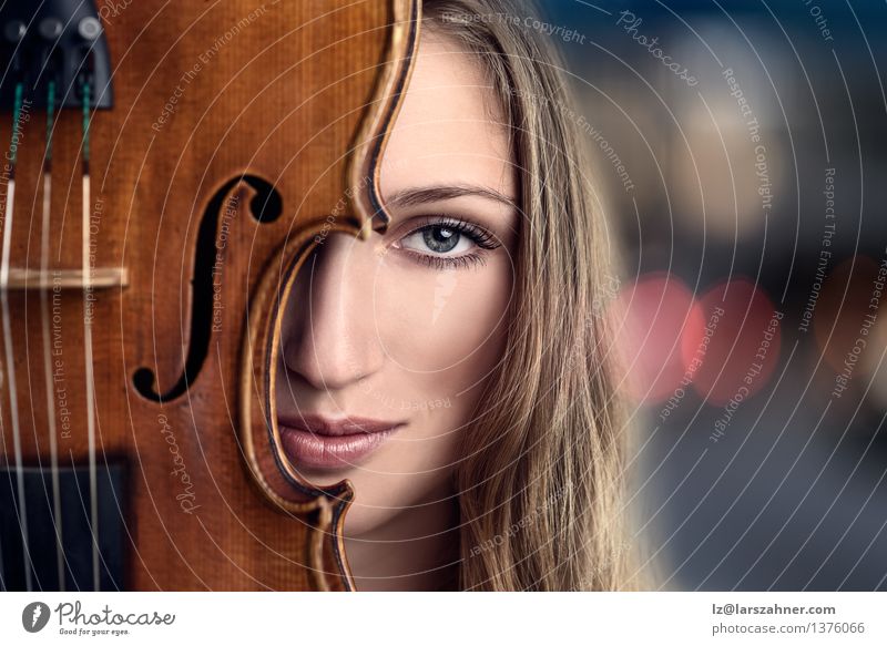 Recht junge Frau, die hinter Violine späht Gesicht Freizeit & Hobby Musik Beruf Erwachsene Musiker Geige blond Lächeln Freundlichkeit blau attraktiv