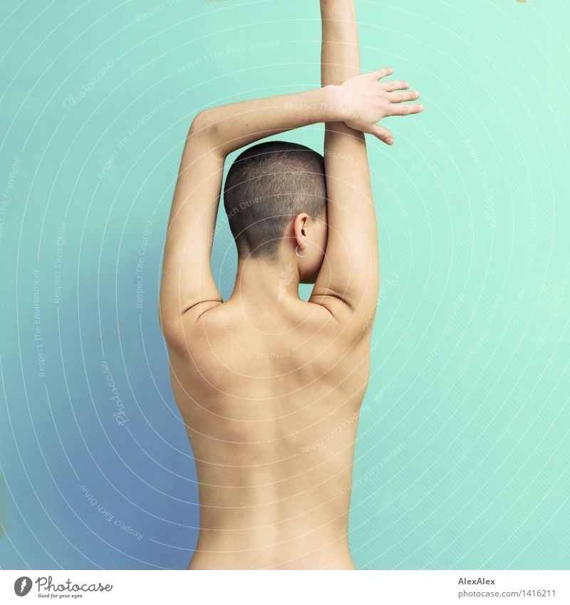 junge Frau mit sehr kurzen Haaren steht in einer Pose mit halb erhobenen Armen nackt vor einer helltürkisen Wand sportlich Fitness harmonisch Wohlgefühl