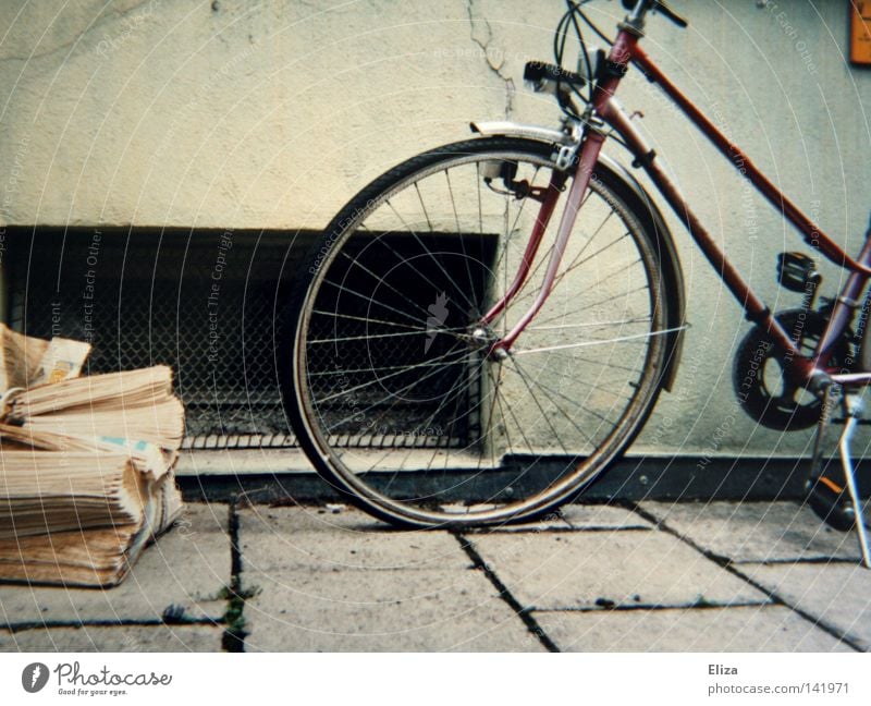 liegengelassen Bürgersteig Fahrrad Zeitung alt vergilbt Reifen Speichen Gitter Wand fließen Haus parken Zeitschrift Ausschnitt. Kellerfenster absetzen