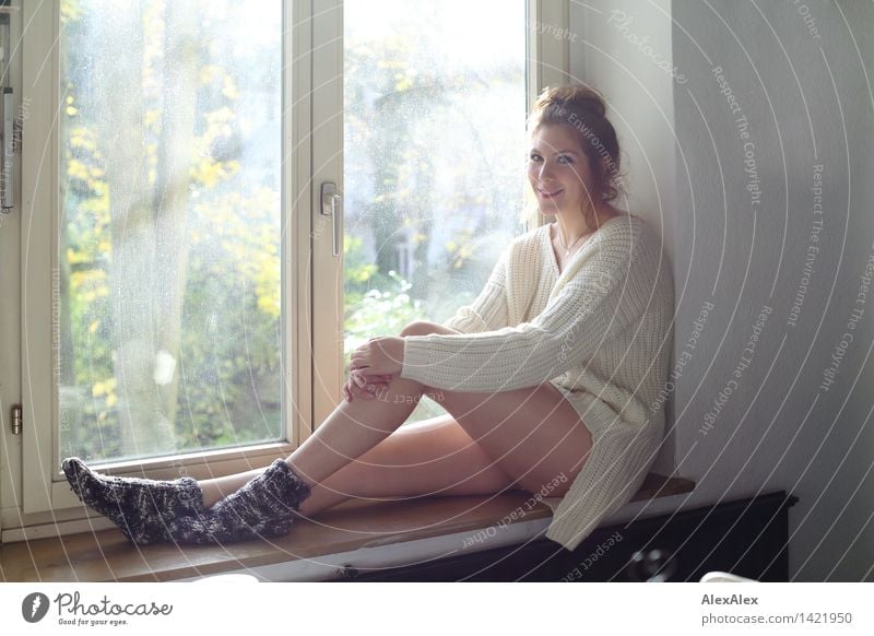 Junge Frau sitzt auf der Fensterbank in sonnenlichtdurchfluteter Küche und lächelt in die Kamera Leben harmonisch Wohlgefühl Jugendliche Gesicht Beine