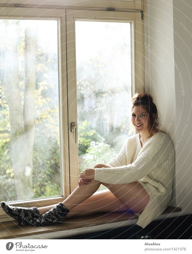 Junge Frau sitzt in sonnenlichtdurchfluteter Küche in der Fensterbank und lächelt in die Kamera Wellness Wohlgefühl Erholung Fensterbrett Jugendliche Gesicht