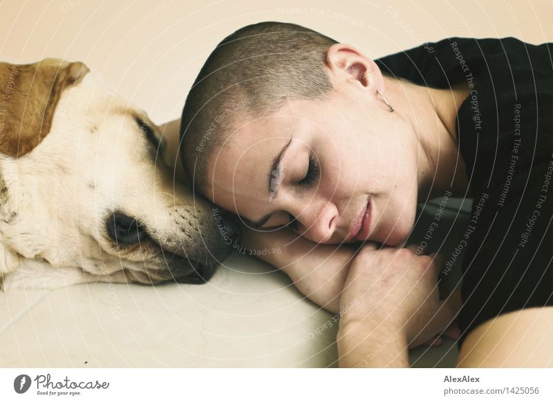 Junge Frau mit sehr kurzen Haaren liegt ruhend mit geschlossenen Augen Kopf an Kopf mit einem jungen, blonden Labrador Wohlgefühl Sinnesorgane Jugendliche