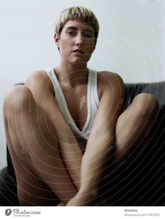Junge, sportliche, schlanke Frau sitzt barfuß in Unterwäsche auf dunkler Couch im Schneidersitz Leben Junge Frau Jugendliche Gesicht Beine 18-30 Jahre