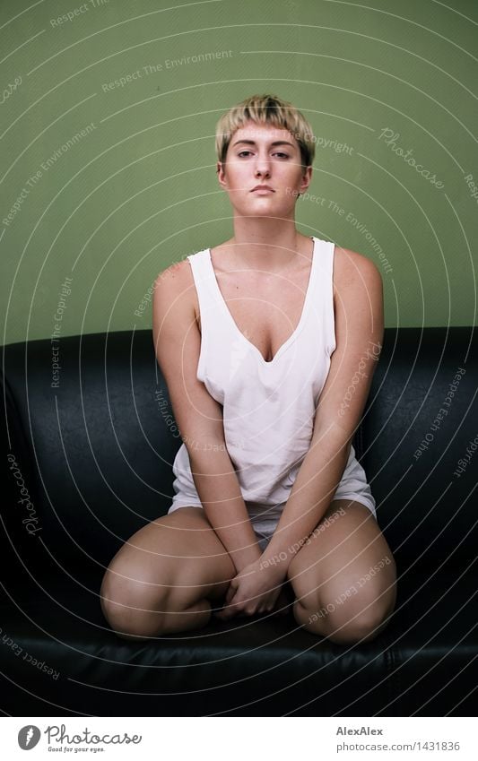 Junge, sportliche, schlanke Frau kniet in Unterwäsche auf dunkler Couch vor grüner Wand harmonisch Erholung ruhig Junge Frau Jugendliche Körper 18-30 Jahre