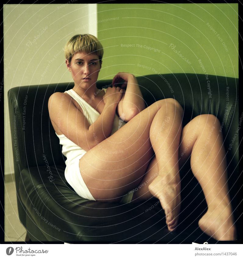 Analoges Bild (6x6) einer jungen Frau, die barfuß in Unterwäsche auf einer dunkeln Couch sitzt und die Beine anzieht Stil Wohlgefühl Erholung Raum Sofa