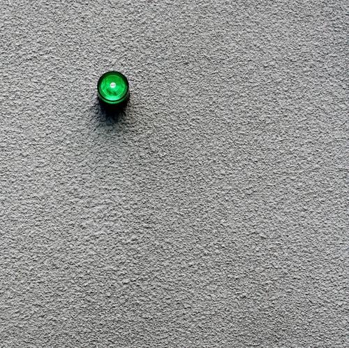 Kleine grüne Alarmleuchte... Alarmanlage Licht Lampe Signal Wand Putz grau trist Außenaufnahme minimalistisch signalisieren Warnsignal Warnleuchte Signalanlage