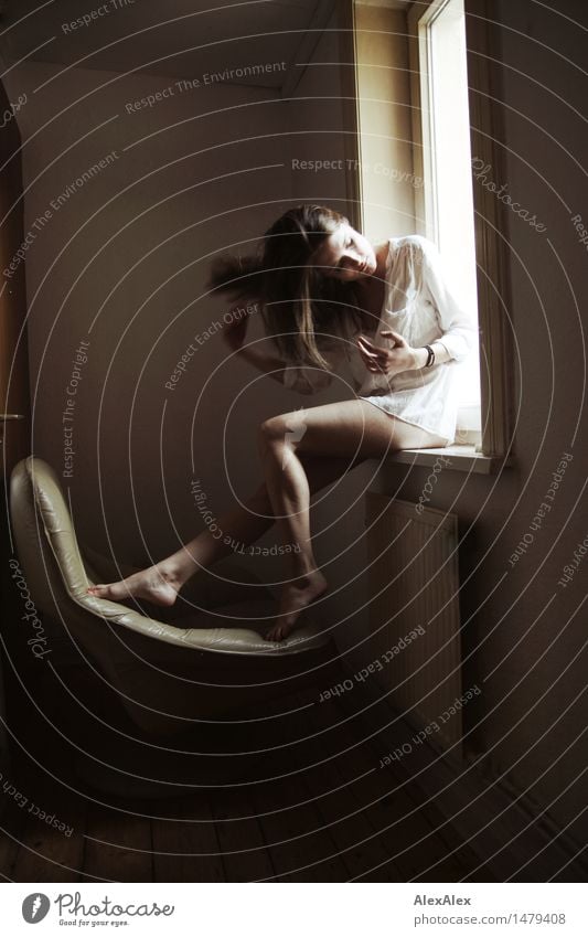 junge Frau sitzt barfüßig in einem Fensterrahmen und fährt sich durch ihre langen, brünetten haare schön Sinnesorgane Erholung Sessel Raum Junge Frau