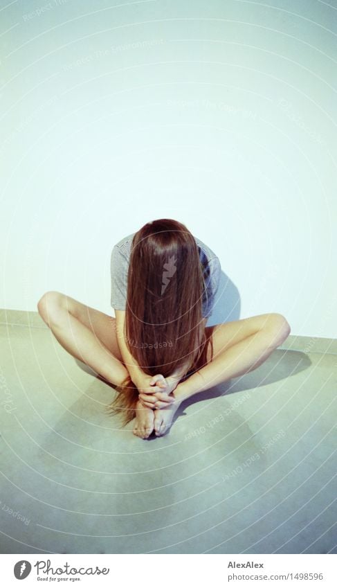 \||/ - junge Frau mit langen, schlanken Beinen sitzt barfuß auf dem Boden mit ausgestreckten Knien und hat den Kopf so gesenkt, dass ihre langen, brünetten Haare den Oberkörper verdecken