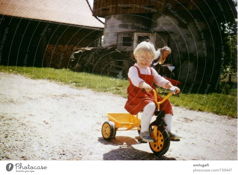 Wheels keep on turning... gelb rot Dreirad Kind blond fahren Bauernhof Hof Brille Kleid Freude Kleinkind Sommer