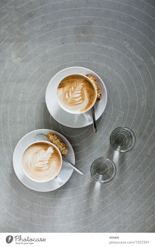 Cappuccinos Kaffee Tasse Milch milchschaum latte art latteart Löffel Keks Licht blur genießen Koffein Tisch grau Beton Gegenlicht braun weiß Feder Frühstück