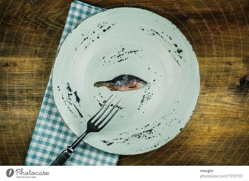 Ein Teller, darauf ein kleiner Fisch, eine Gabel eine Serviette auf einem Holztisch Lebensmittel Ernährung Mittagessen Bioprodukte Diät Fasten Gesundheit Koch