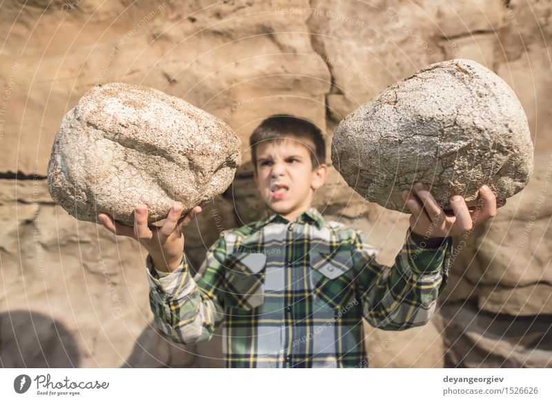 Starkes Kind hält schwere Steine Körper Junge Mann Erwachsene Kindheit Arme Felsen Fitness klein lustig muskulös niedlich stark laden Muskulatur jung Kinder