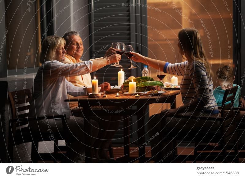 Familie Abendessen im Freien im Hinterhof in ruhigen Abend. Junge Frau und Senior Eltern Toasting mit Wein, während Kind spielt Spiele Gemüse Alkohol Glück