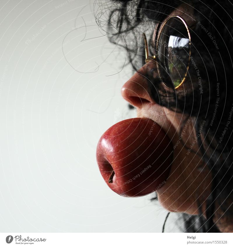 Nahaufnahme eines weiblichen Gesichts mit einer Sonnenbrille und schwarzen Haaren und einem ganzen Apfel im Mund Lebensmittel Bioprodukte Mensch feminin Frau