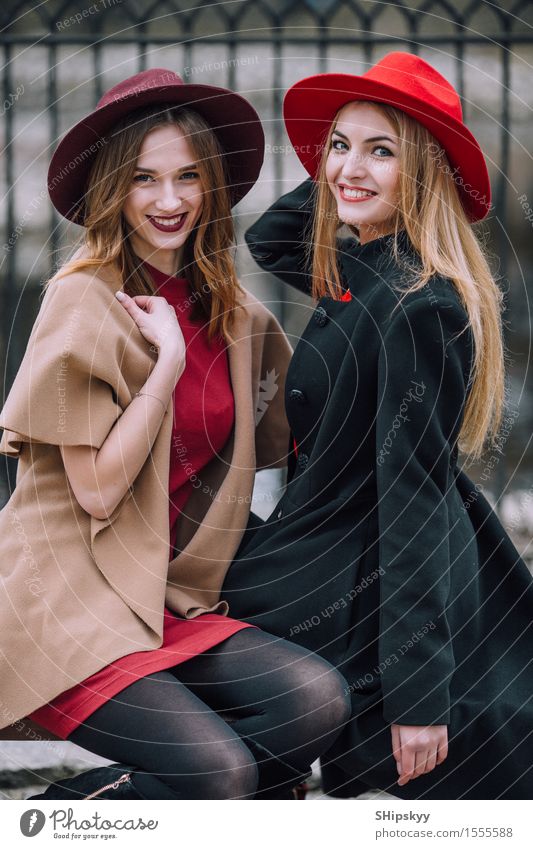 Zwei Mädchen, die auf der Bank und dem Lächeln sitzen Lifestyle Freude Glück schön Gesicht Sitzung Mensch feminin Frau Erwachsene Freundschaft Herbst Mode Hut