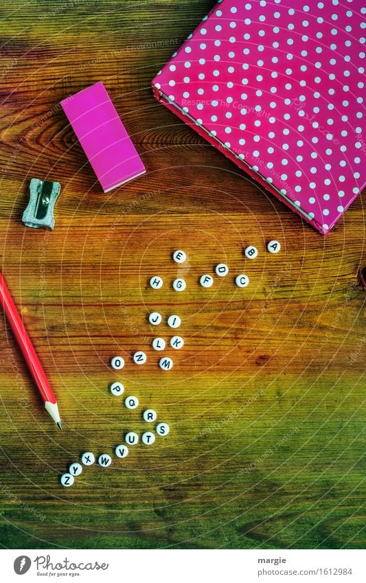 Alphabet mit weißen Buchstaben, ein Heft und Radiergummi in pink, ein roter Bleistift und ein Spitzer auf einem Holztisch Freizeit & Hobby Bildung Schule lernen