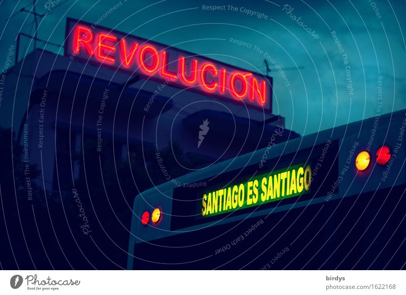 Leuchtschrift " revolucion " auf einem Gebäude in Santiago de Cuba. Im Vordergrund ein Linienbus mirt der Leuchtschrift " Santiago es Santiago " ein Ausspruch von Fidel Castro über die besonderheit von Santiago de Cuba
