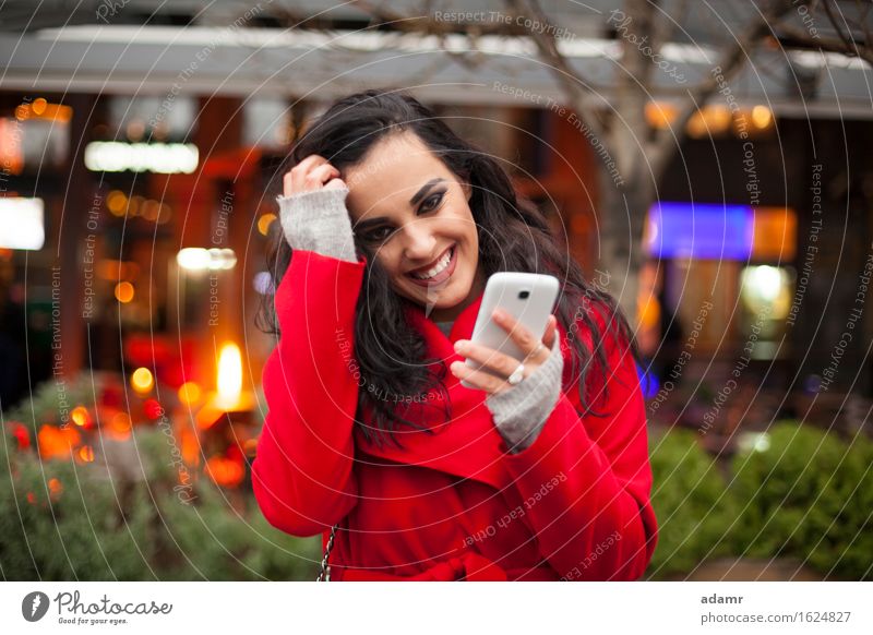 Schöne lächelnde Frau in rotem Mantel mit Mobiltelefon in der Hand, Smartphone, Stadtszene Telefon Lächeln Lifestyle Mädchen Mobile Person kalt Winter