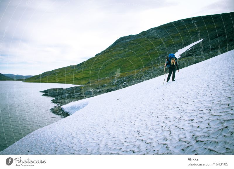 Junge Wanderin mit Rucksack und einem hölzernen Wanderstock überquert vorsichtig eine Gletscherzunge in den norwegischen Bergen am Steilhang Abenteuer Sport