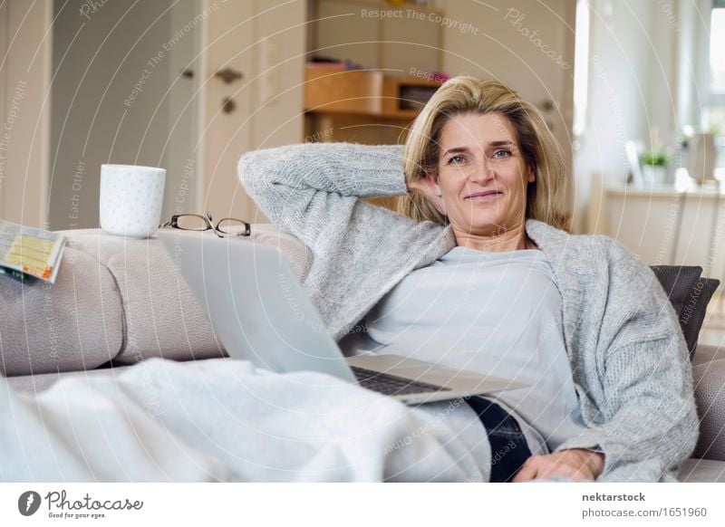 Blonde Frau, die vom Wohnzimmer aus arbeitet. Lifestyle Freude Zufriedenheit Erholung Freizeit & Hobby Ferien & Urlaub & Reisen Sofa Computer Notebook Internet