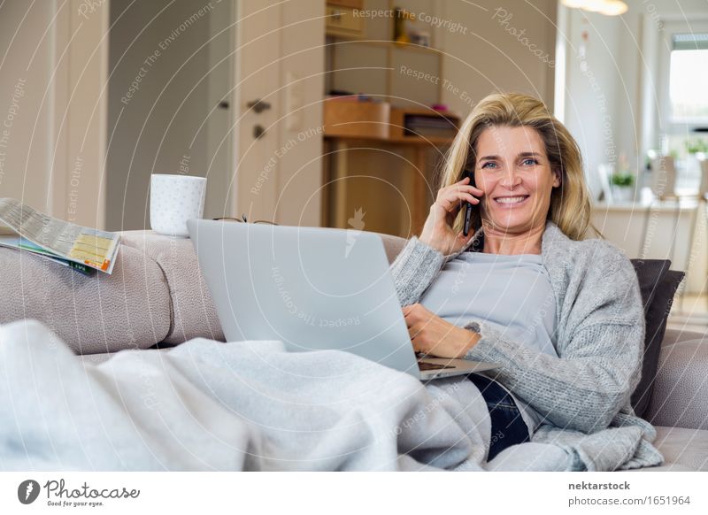 Blonde Frau, die vom Wohnzimmer aus arbeitet. Lifestyle Glück Erholung Freizeit & Hobby Ferien & Urlaub & Reisen Sofa sprechen Telefon Computer Notebook