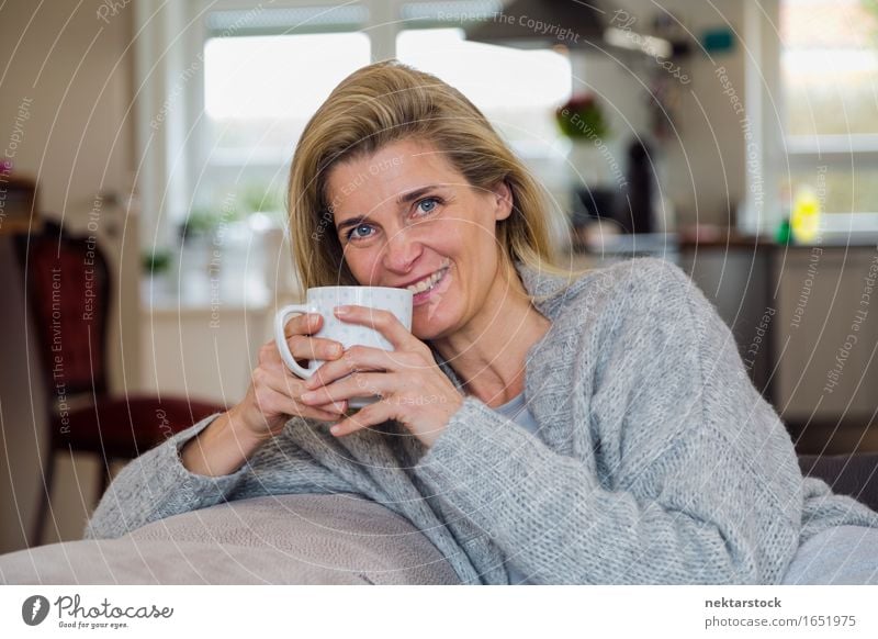 Attraktive blonde Frau, die sich zu Hause entspannt. Getränk Kaffee Lifestyle Freude Glück Zufriedenheit Erholung Freizeit & Hobby Sofa Erwachsene Lächeln