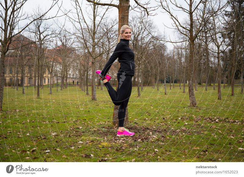 Frau, die das rechte Bein im Park streckt. Lifestyle Körper Wellness ruhig Winter Sport Mensch Erwachsene Baum Fitness Lächeln stehen sportlich dünn