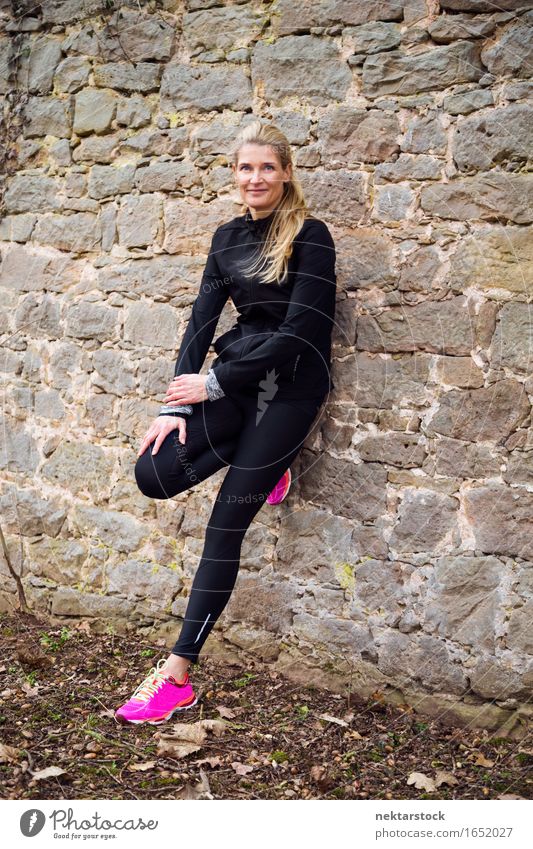 Porträt einer Frau, die sich an eine Wand im Park lehnt. Lifestyle Glück Körper Wellness Sport Mensch Erwachsene Stein Fitness Lächeln sportlich dünn
