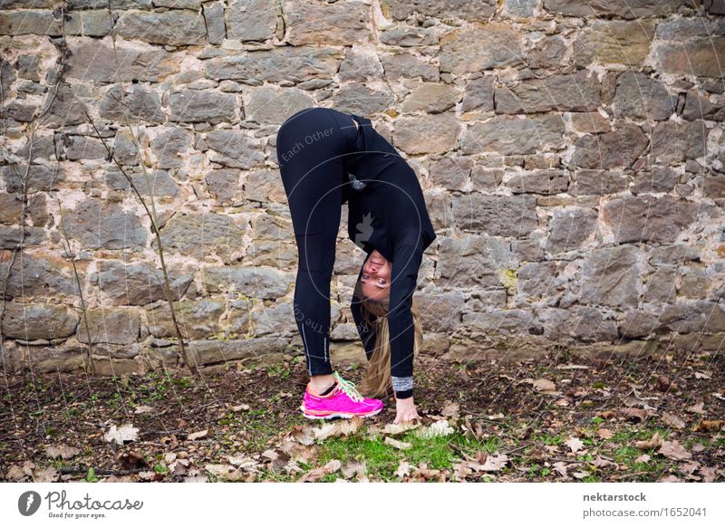 Frau, die ihren Körper vor der alten Mauer im Park ausstreckt. Lifestyle Glück Wellness Sport Mensch Erwachsene Stein Fitness Lächeln sportlich Freundlichkeit