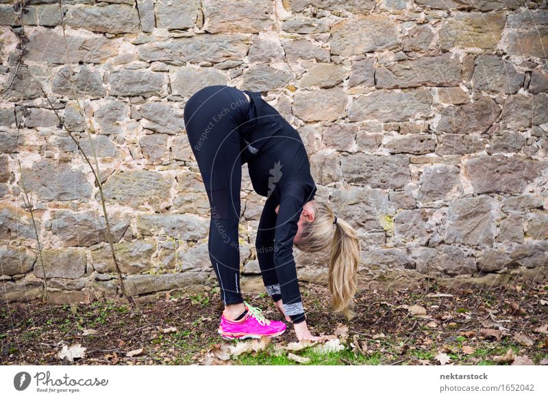 Frau, die ihren Körper vor der alten Mauer im Park ausstreckt. Lifestyle Glück Wellness Sport Mensch Erwachsene Stein Fitness Lächeln sportlich Freundlichkeit
