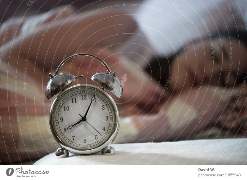 schlafende junge Frau mit Wecker im Vordergrund der nach 8 Uhr anzeigt verschlafen langschläfer Langschläferin Uhrzeit 5 nach fünf nach verspätung übermüdet